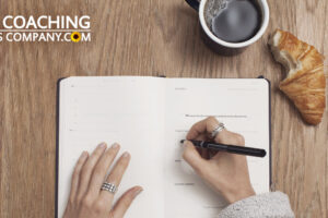 Hands journaling around leadership questions at desk with coffee